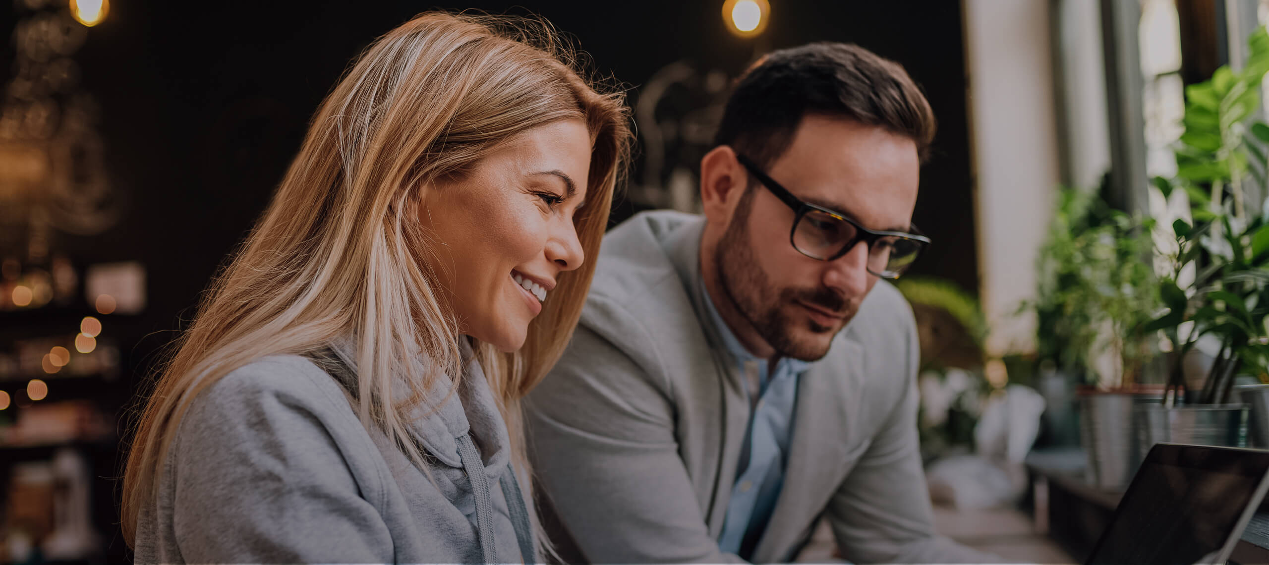 Zwei Personen sitzen an einem Tisch und blicken in einen Laptop. Die Person, die direkt vor dem Laptop sitzt, tippt aktiv.